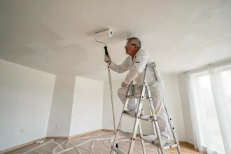 Peintre professionnel appliquant de la peinture glycéro blanche au plafond avec un rouleau à long manche sans ponçage préalable